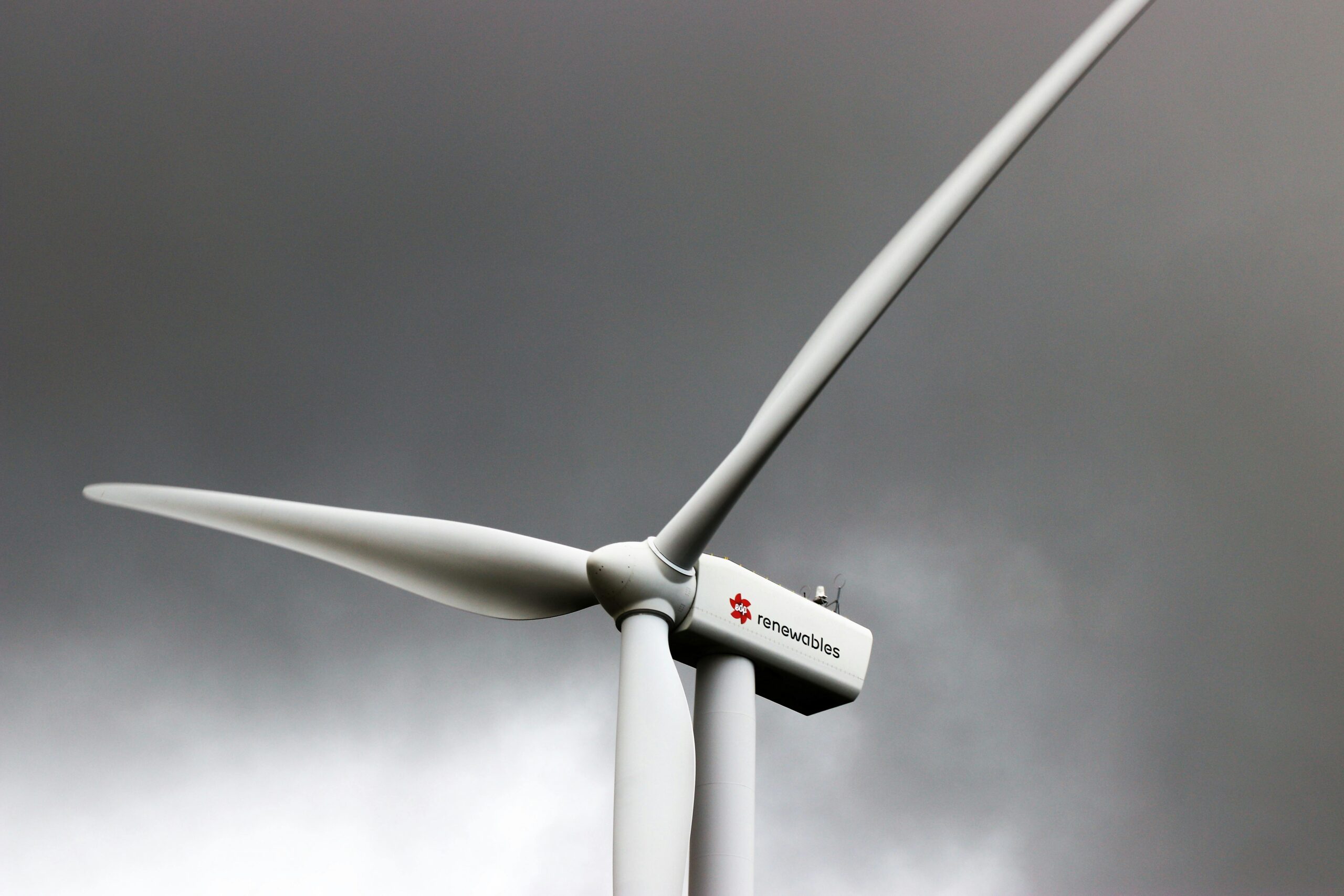 A wind turbine stands tall against dark, cloud-laden skies, symbolizing renewable energy.